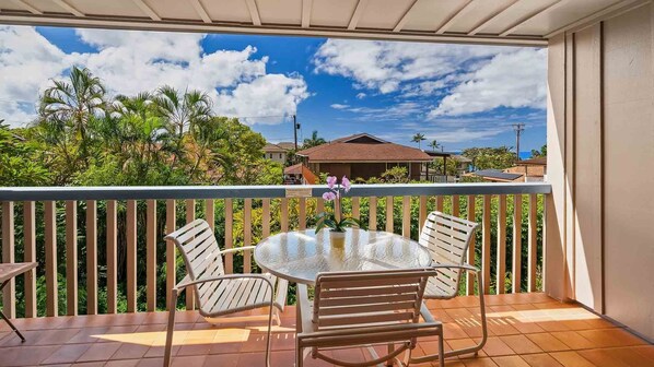 A balcony with a round table and four chairs, overlooking a residential area with houses and greenery.