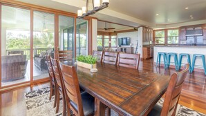 A spacious dining area with a wooden table and chairs, a ceiling fan, and a kitchen in the background. - Family house near Hanalei with ocean views (Princeville)