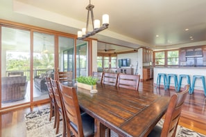 Enjoy meals in this dining area with a large table and chairs, surrounded by sliding glass doors offering a view of lush greenery.