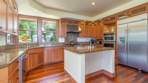 A modern kitchen with wooden cabinets, granite countertops, a stainless steel refrigerator, and a large island. - Family house near Hanalei with ocean views (Princeville)