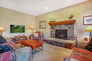 A cozy living room with a stone fireplace, comfortable seating, and a television mounted on the wall.