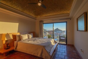 Ein Hotelzimmer mit Bett, Nachttisch, Deckenventilator und einem großen Fenster mit Blick auf die Stadt.