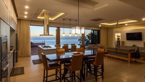 Eine moderne Küche mit Meerblick, ein Essbereich mit einer großen Kochinsel und ein Wohnzimmer mit Fernseher und Sitzgelegenheiten.