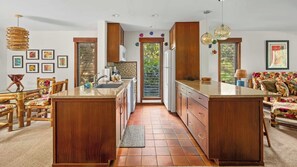 A kitchen with a central island, wooden cabinets, and a dining area with a table and chairs. - Waikomo Stream Villas #403 By Parrish Kauai: bright, updated end-unit w/ dining (Koloa)