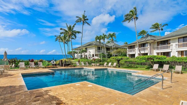 A pool area with lounge chairs and a view of the ocean.
