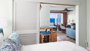 A hotel room with a bed, a dining area with wicker furniture, a view of the ocean, and a ceiling fan. - Poipu Palms #203 By Parrish Kauai: pristine, updated oceanfront gem w/ sunsets & (Koloa)