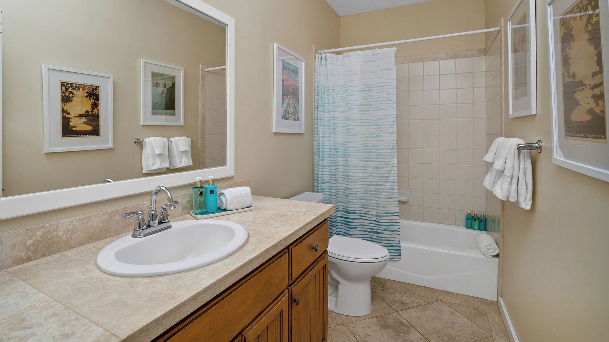 A bathroom with a sink, toilet, and bathtub. There are framed pictures on the wall, a shower curtain, and towels hanging on the wall.
