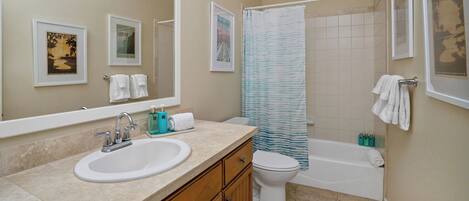 A bathroom with a sink, toilet, and bathtub. There are framed pictures on the wall, a shower curtain, and towels hanging on the wall.