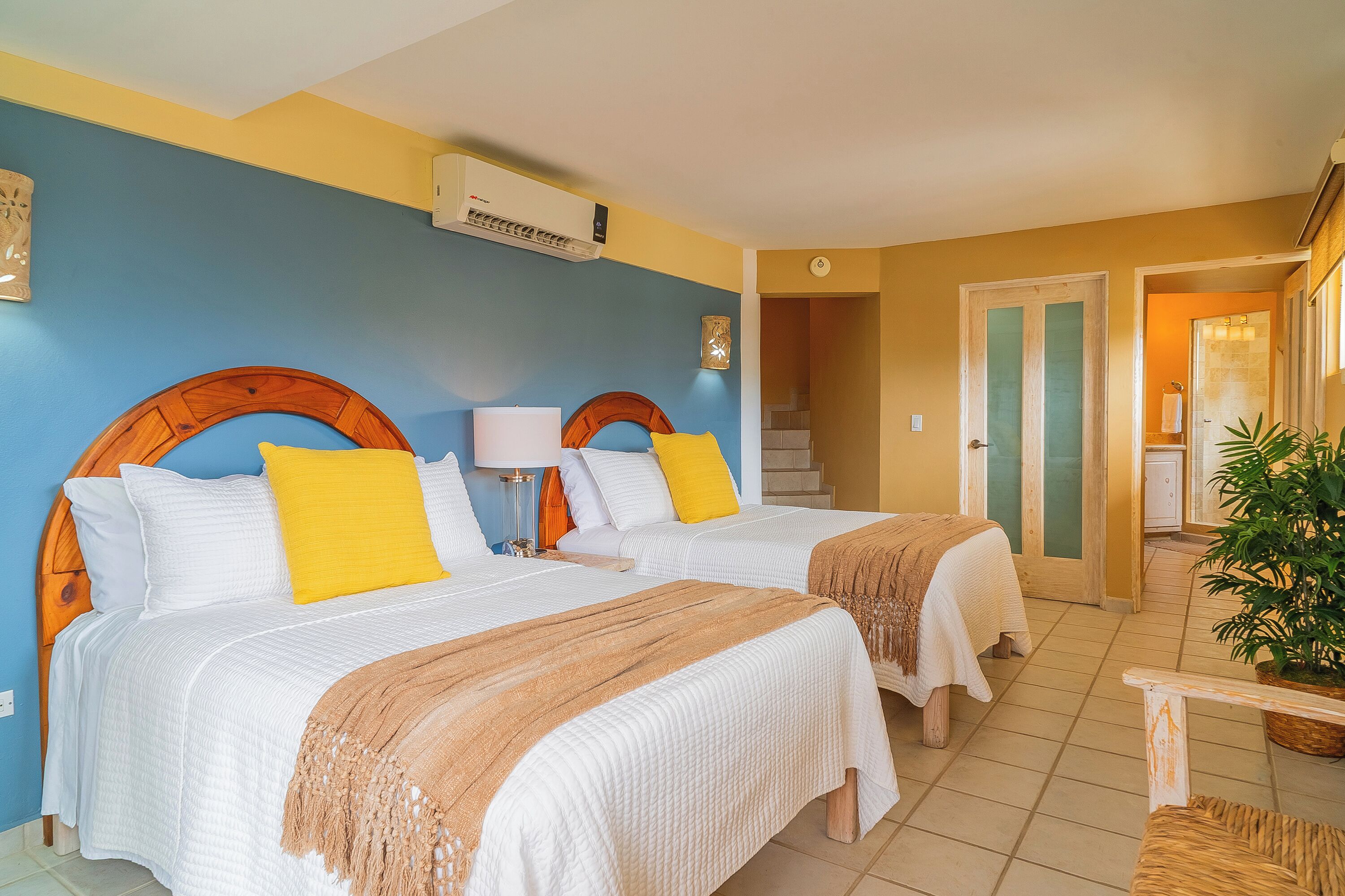 Une chambre d’hôtel avec deux lits, une tête de lit en bois, un climatiseur fixé au mur et un escalier menant à une autre pièce.
