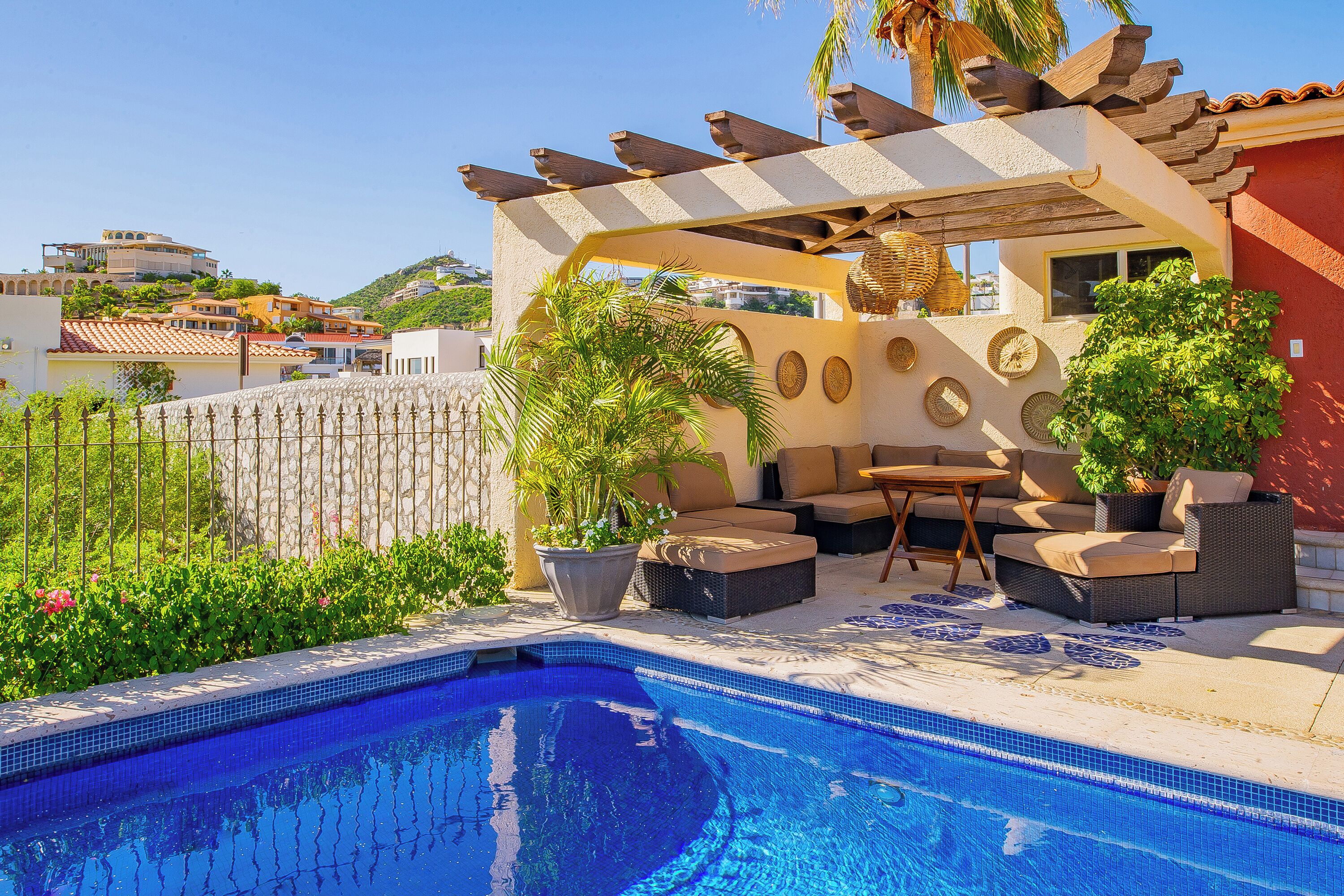 Un área de piscina con pérgola, mobiliario exterior y plantas en macetas.