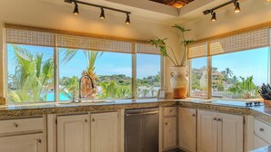 Una cocina con lavavajillas, ventanas amplias y vistas a palmeras y una piscina.