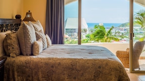 Ein Schlafzimmer mit einem großen Bett, einer Lampe und Blick auf das Meer und die Stadt vom Balkon aus.