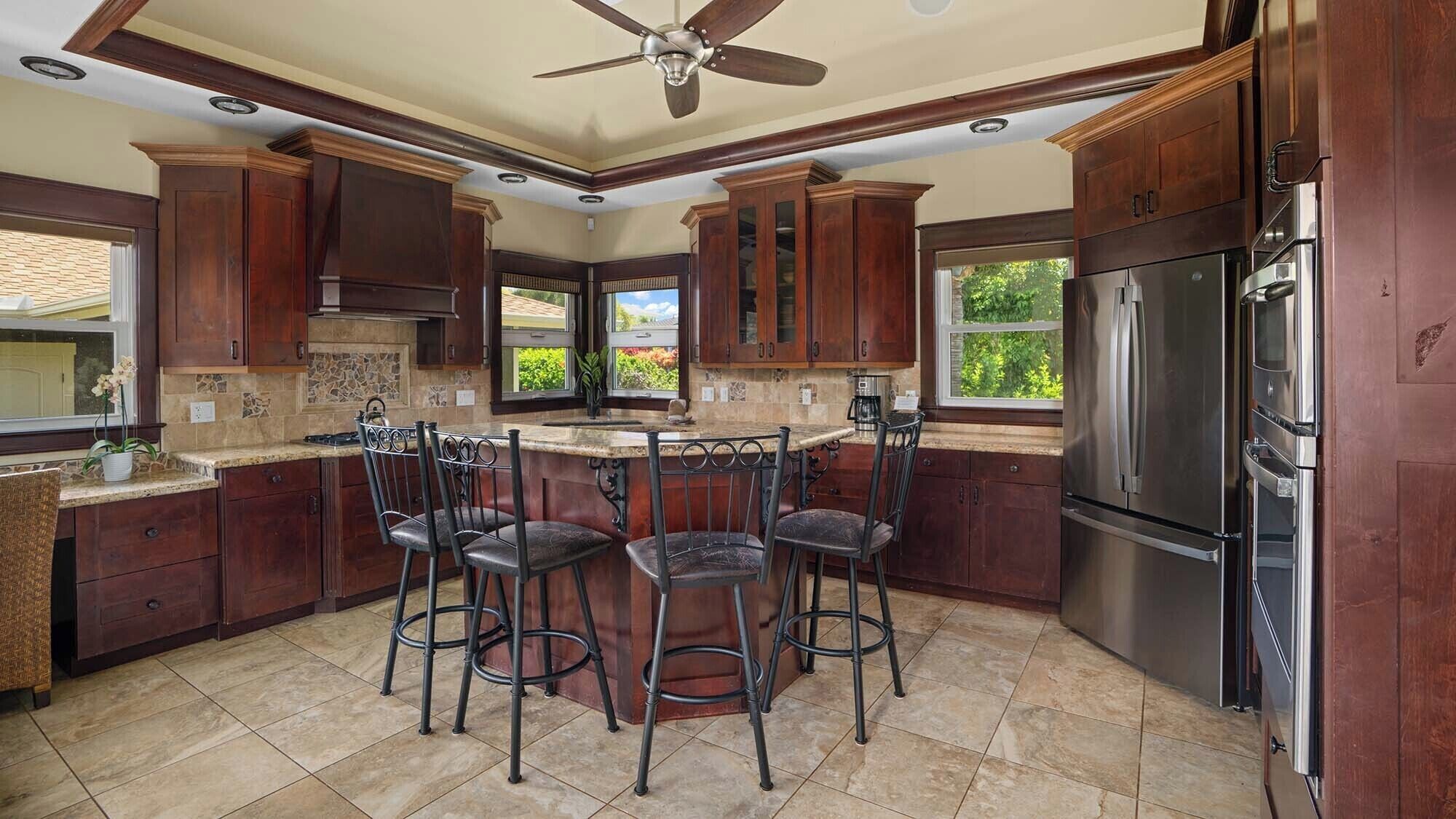 A kitchen with dark wooden cabinets, a stainless steel refrigerator, and a bar area with stools.