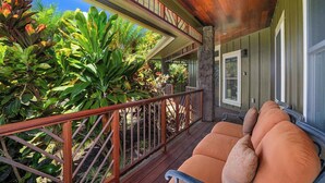 Una terraza de madera con un pilar de piedra, un espacio de descanso al aire libre con cojines y exuberante follaje tropical.