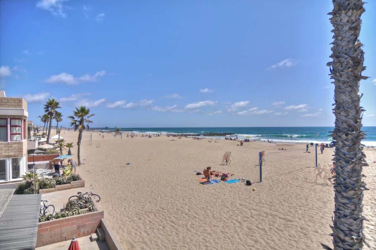 A beach with a building on the left, palm trees, and people relaxing on the sand.