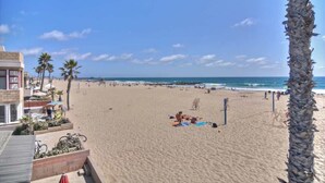 Une plage avec un bâtiment sur la gauche, des palmiers et des personnes se relaxant sur le sable.