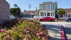 Une vue de rue avec une voiture de sport rouge garée devant un bâtiment vert, orné d’une clôture blanche et d’un petit porche.