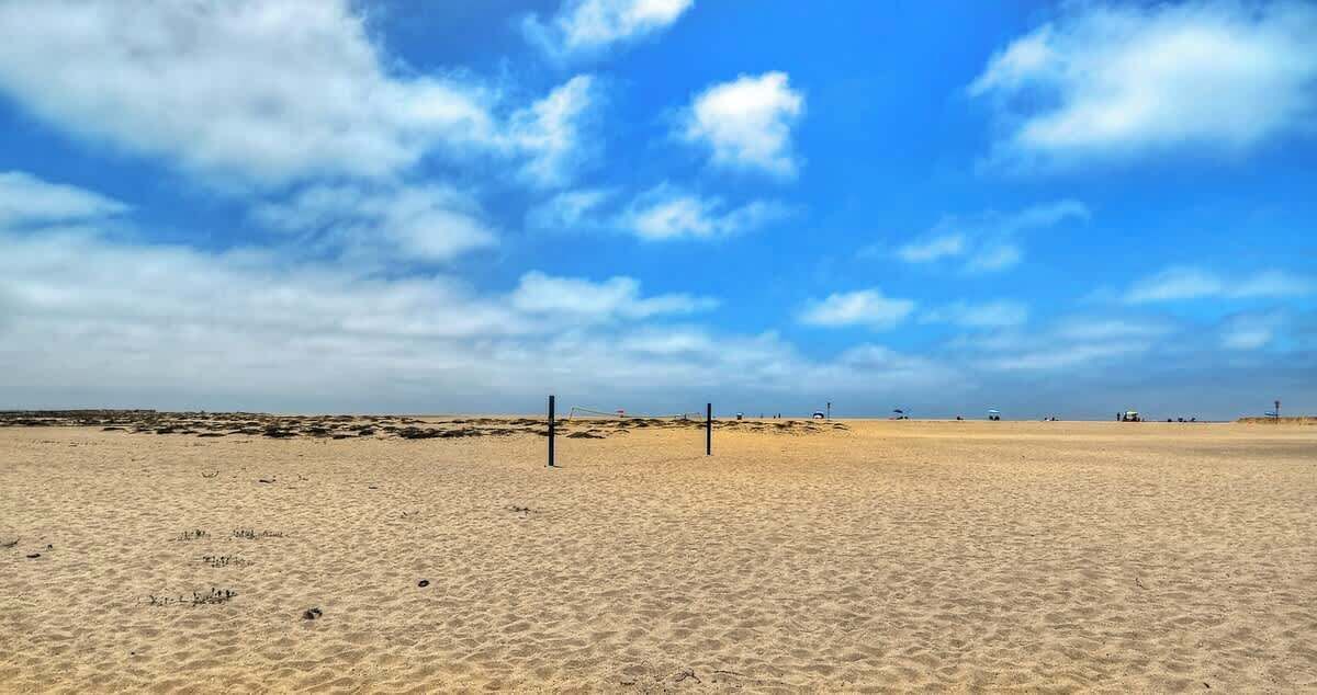 A wide sandy beach with a clear sky and a few scattered clouds.