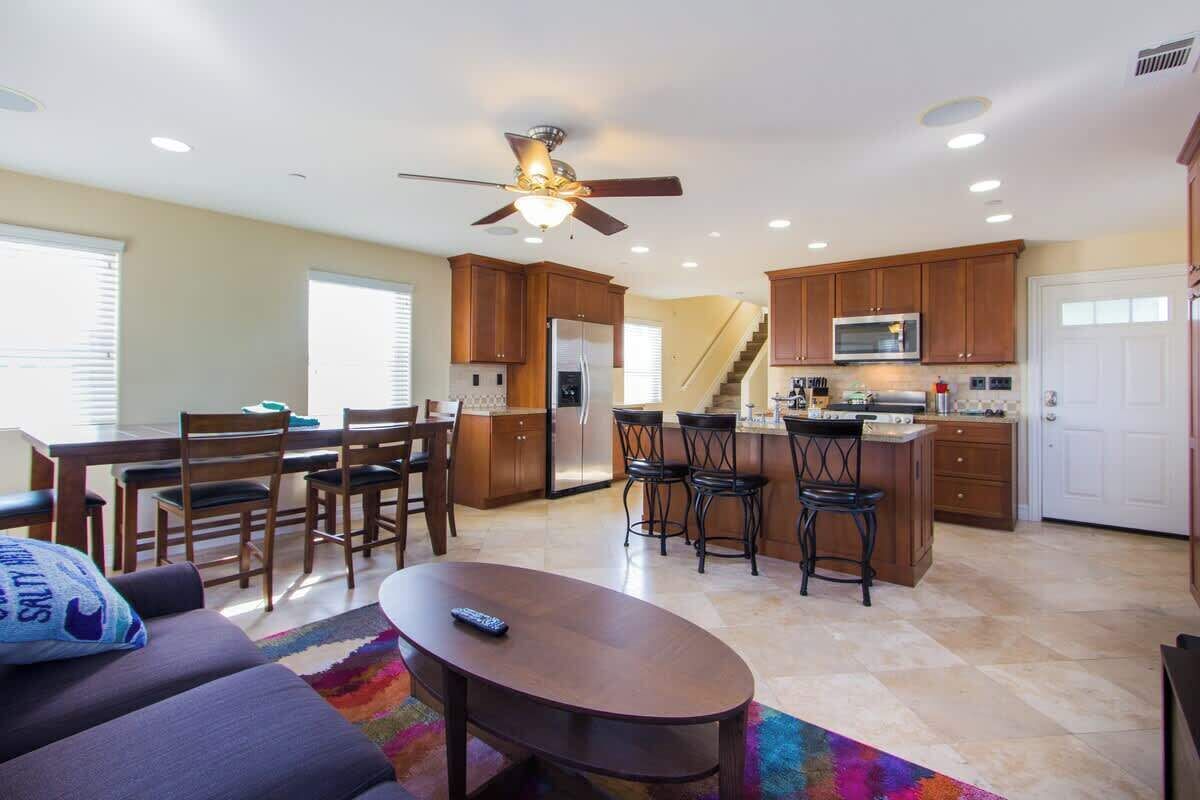 A spacious kitchen with wooden cabinets, a central island with bar stools, a ceiling fan, and a dining area with a table and chairs.