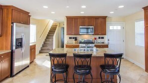 Une cuisine avec des meubles de rangement en bois, un réfrigérateur en acier inoxydable, un four à micro-ondes, une cuisinière et trois tabourets de bar.