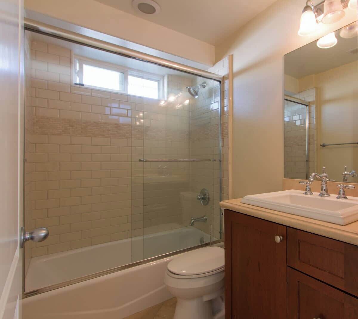 Een badkamer met een douchecabine van glas, een wit toilet en een wastafel met spiegel.