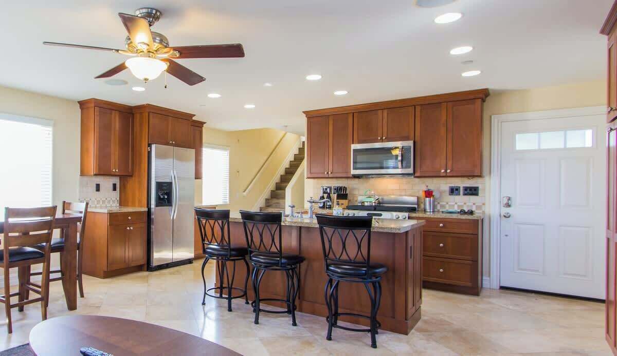 A spacious kitchen with wooden cabinets, a stainless steel refrigerator, a microwave, and a bar area with stools.