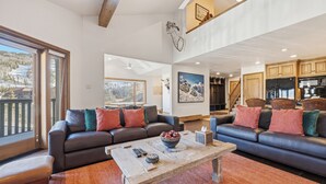 A spacious living room with a large sofa, a coffee table, and a view of a snowy landscape through a sliding door. - Luxury Penthouse w Amazing Mountain Views, W404 (Vail)