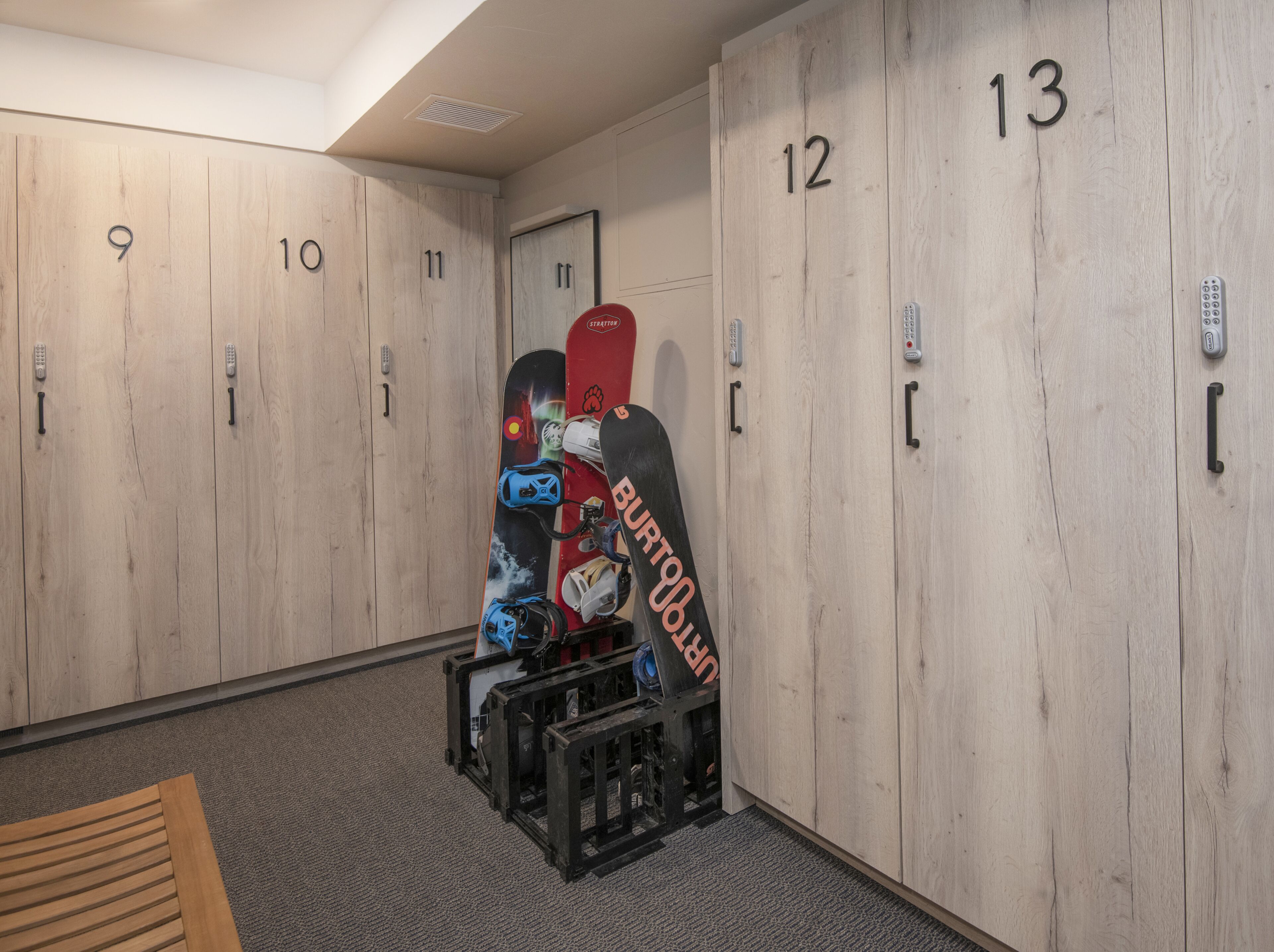 A locker room with numbered lockers from 9 to 13, a bench, and a snowboard leaning against the wall.