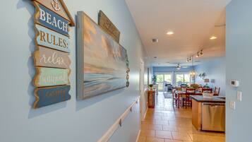 A hallway with a wooden sign reading "BEACH RULES: relax enjoy," a large abstract painting, and a kitchen area with a dishwasher.
