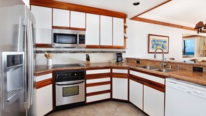 A modern kitchen with stainless steel appliances, wooden cabinetry, and a granite countertop.