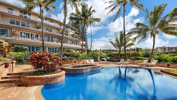 Un resort con una gran piscina, palmeras y un edificio de varios pisos con balcones.