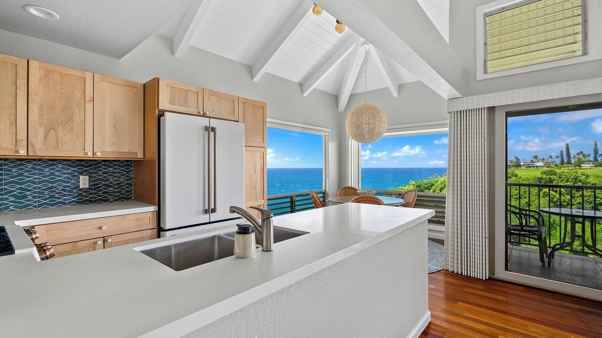 A modern kitchen with a large island, wooden cabinets, and a view of the ocean.