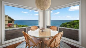 Zona pranzo con tavolo in vetro e sedie in vimini, con vista panoramica sull'oceano.