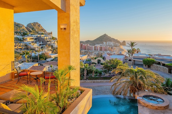 A balcony with a pool, outdoor seating, and a view of the beach and cityscape.
