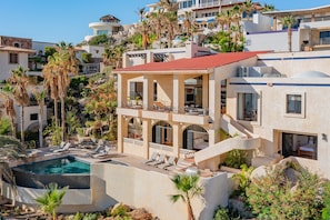 A multi-story building with a pool, outdoor seating, and a staircase leading to a balcony.