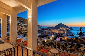 A terrace with outdoor seating and a view of a coastal town at dusk.