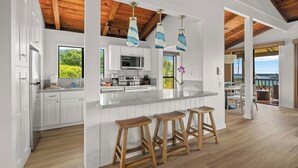 A modern kitchen with white cabinetry, a large island with bar stools, and a view of the ocean.