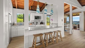 Cozinha moderna com armários brancos, uma ilha grande com banquetas e vista para o oceano.