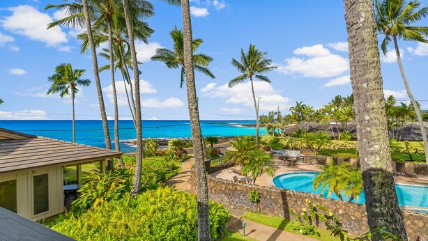 A resort with a pool, palm trees, and a view of the ocean.