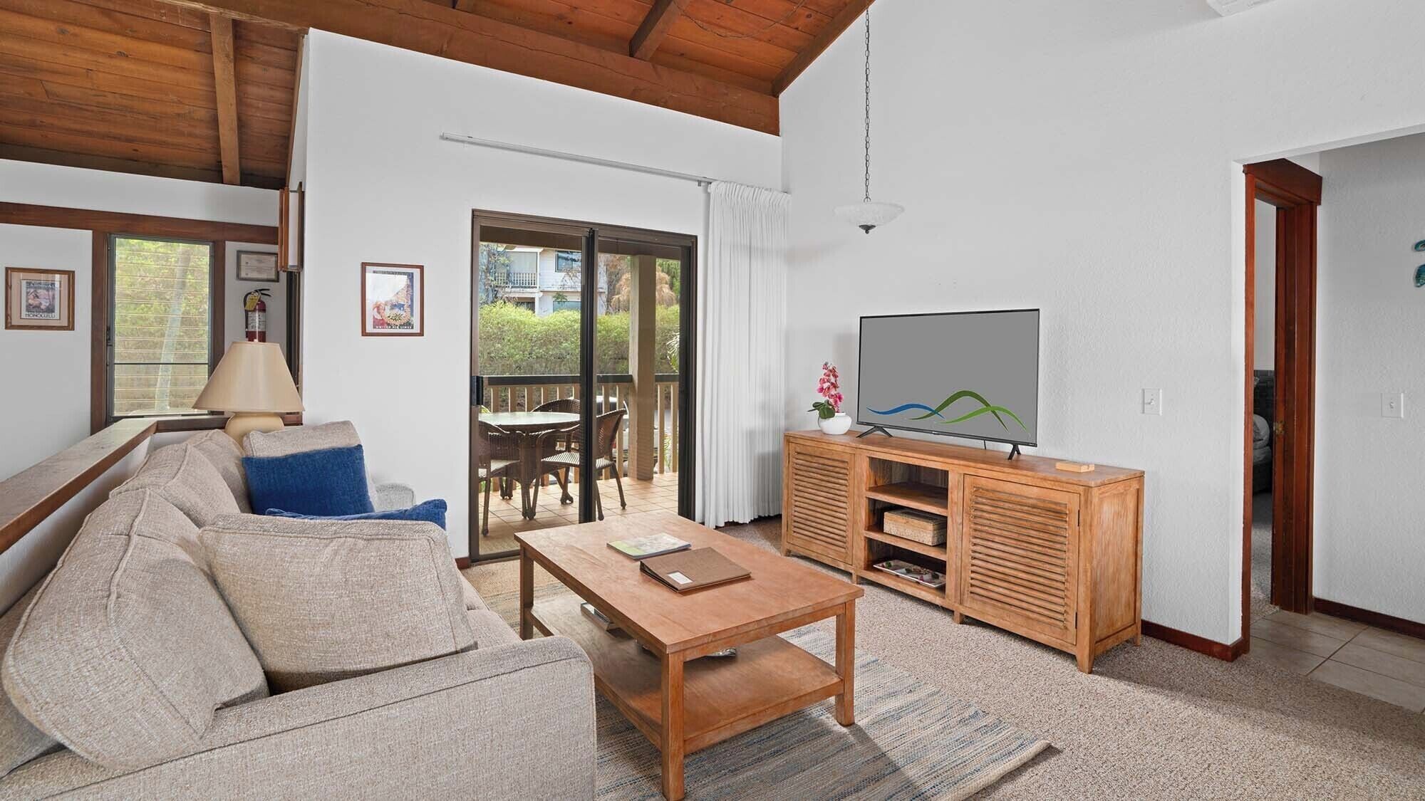 A living room with a sofa, coffee table, TV, and a balcony with a table and chairs.