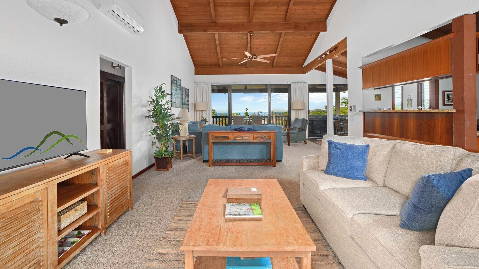 Ett rymligt vardagsrum med ett träpanelat tak, en tv, en soffa, ett soffbord och utsikt över havet.