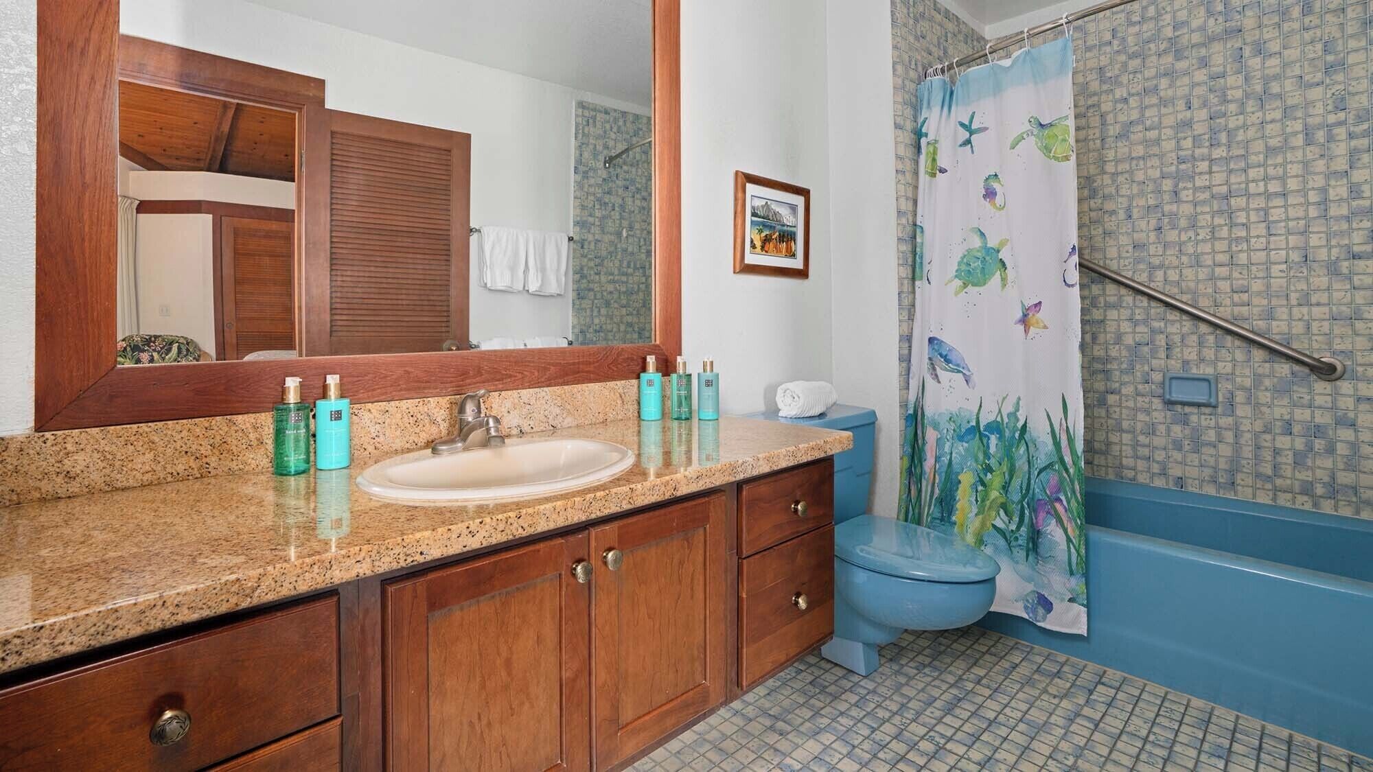 A bathroom with a wooden vanity, a sink, a mirror, a toilet, and a shower curtain with sea creatures.