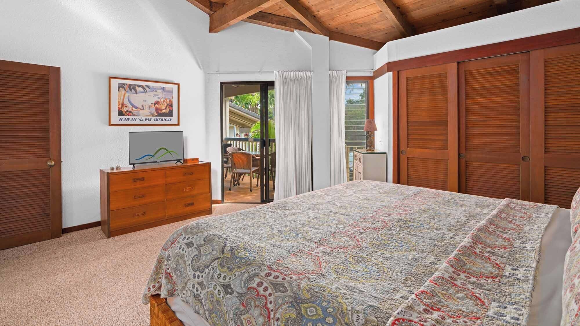 A bedroom with a bed, wooden wardrobe, a dresser, a television, and a door leading to an outdoor area.