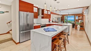 Una cocina moderna con una isla grande, electrodomésticos de acero inoxidable, armarios de madera e iluminación colgante.