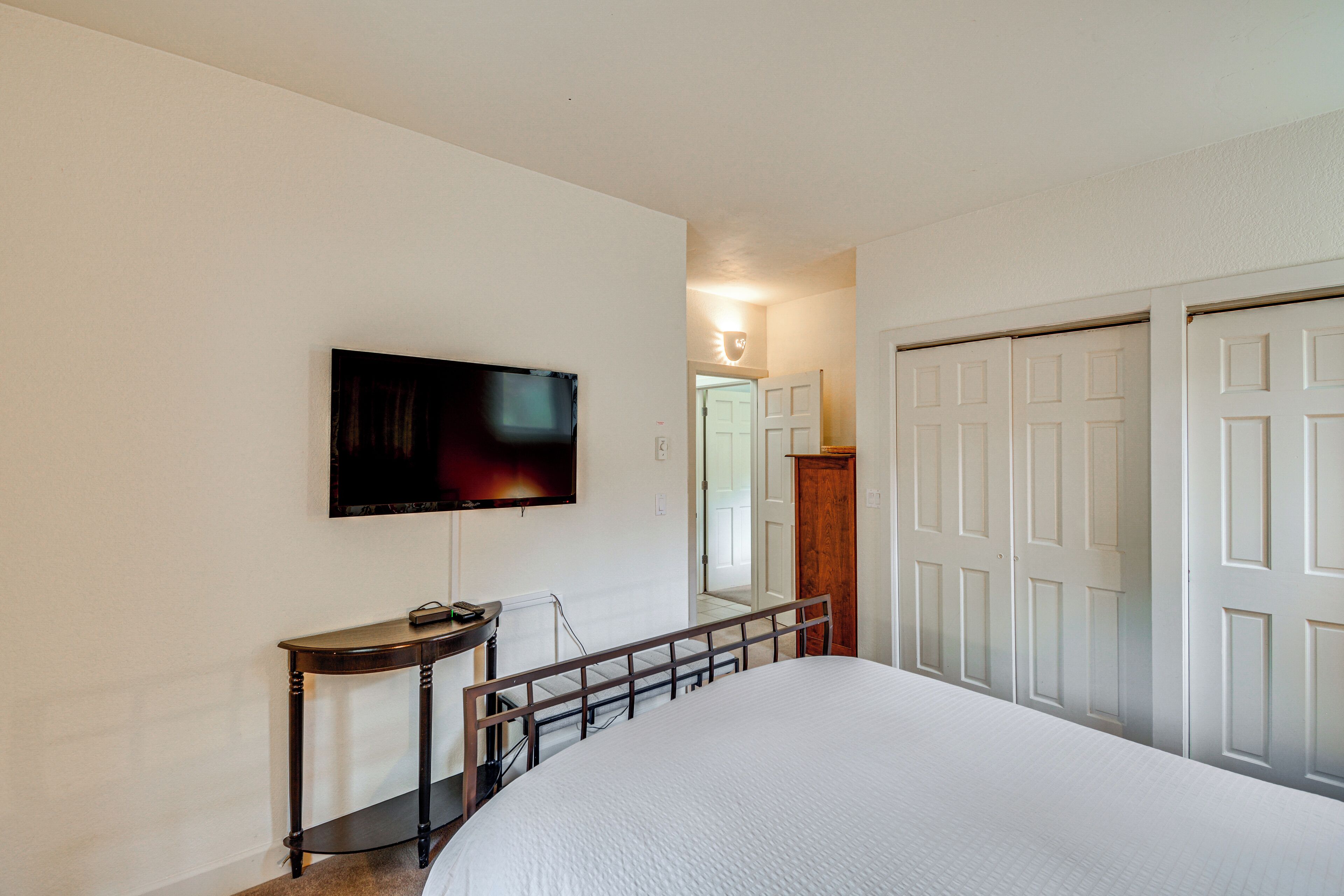 A bedroom with a large bed, a television mounted on the wall, a small table, and a wardrobe with multiple doors.