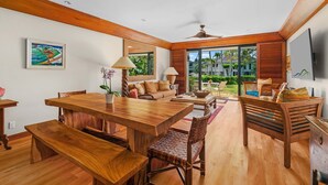 A spacious living area with a wooden dining table, comfortable seating, and a large sliding glass door leading to a balcony.