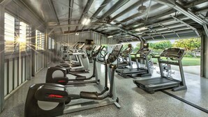 Een sportschool met meerdere loopbanden en fitnessapparatuur, grote ramen en uitzicht op groen.