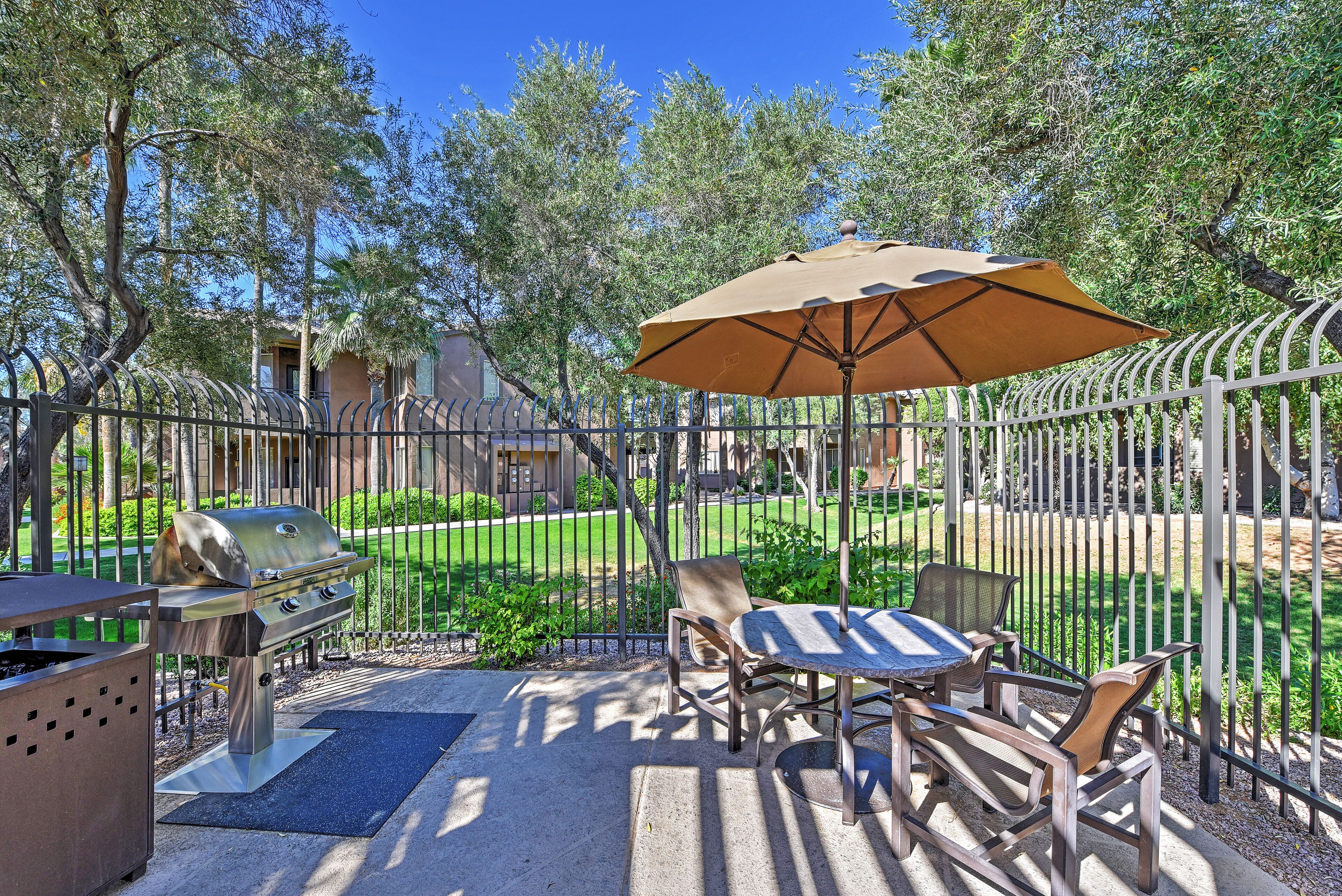 An outdoor patio with a grill, a table, chairs, and an umbrella.
