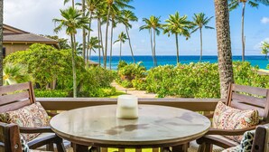 Una mesa redonda con una vela, rodeada de sillas de madera con cojines estampados, con vistas a un jardín tropical con palmeras y al océano.