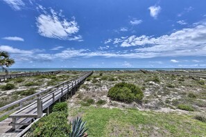 Une promenade en bois menant à une plage, avec un ciel dégagé et quelques nuages.